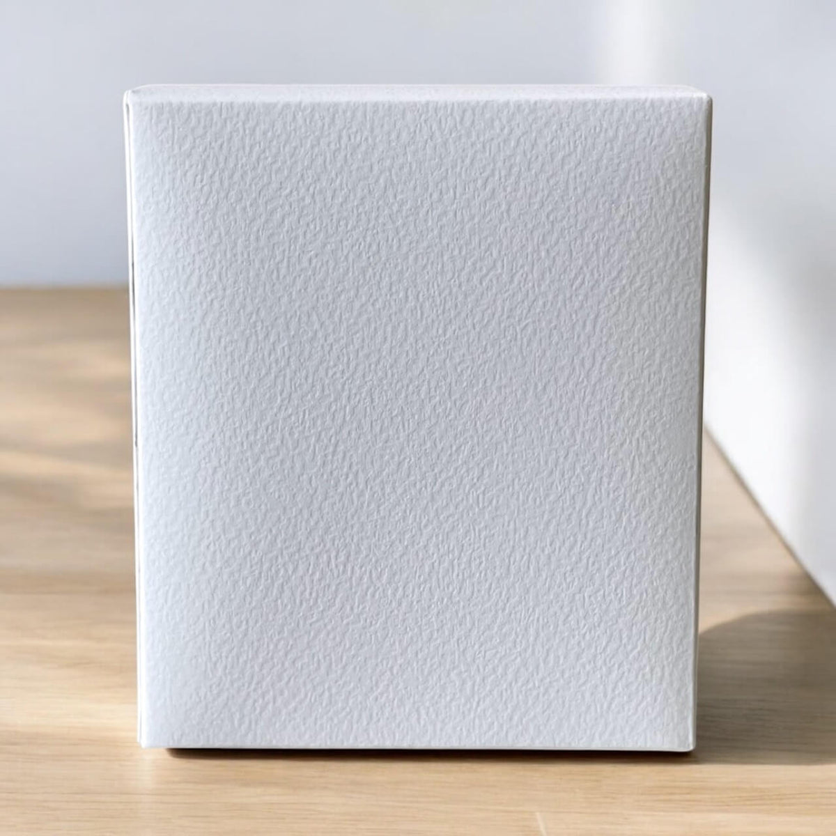 White textured box on a wooden surface with a light gray background