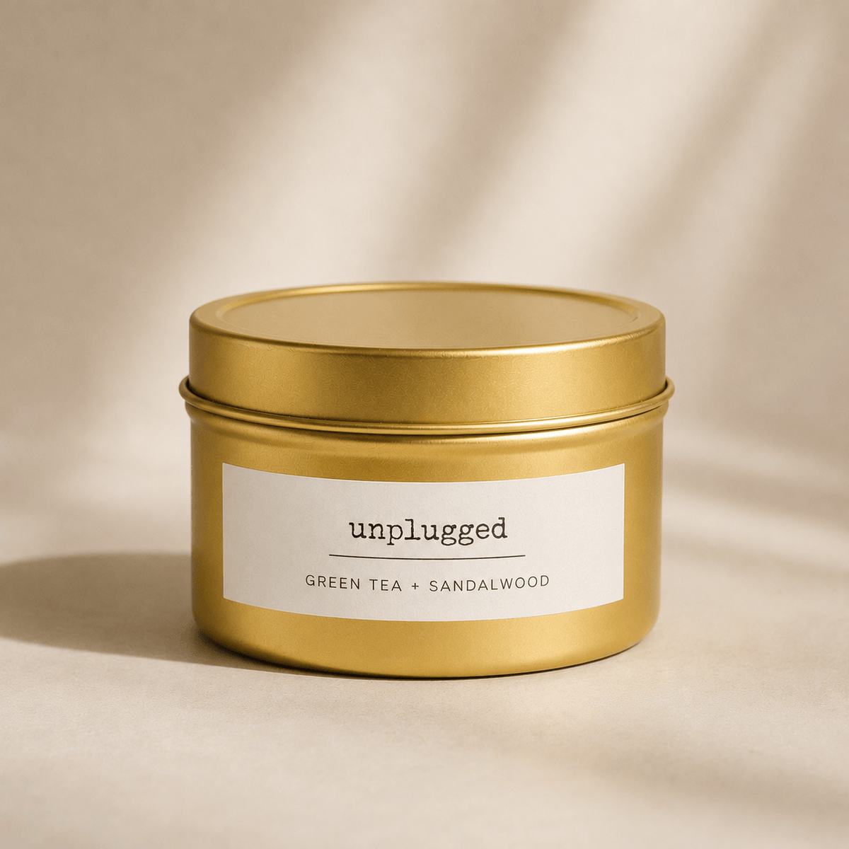Gold candle tin labeled 'unplugged' with 'Green Tea + Sandalwood' on a beige background